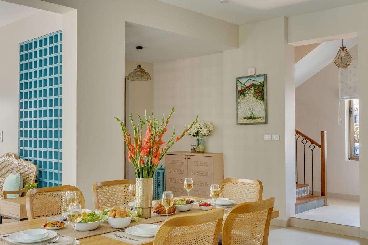 Dining area with cane chairs and fresh flowers, staircase beyond